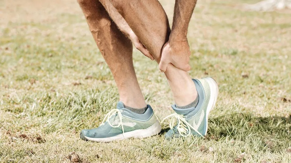 Coureur massant son tendon d'Achille au bord d'un chemin, lumière naturelle et tenue de sport